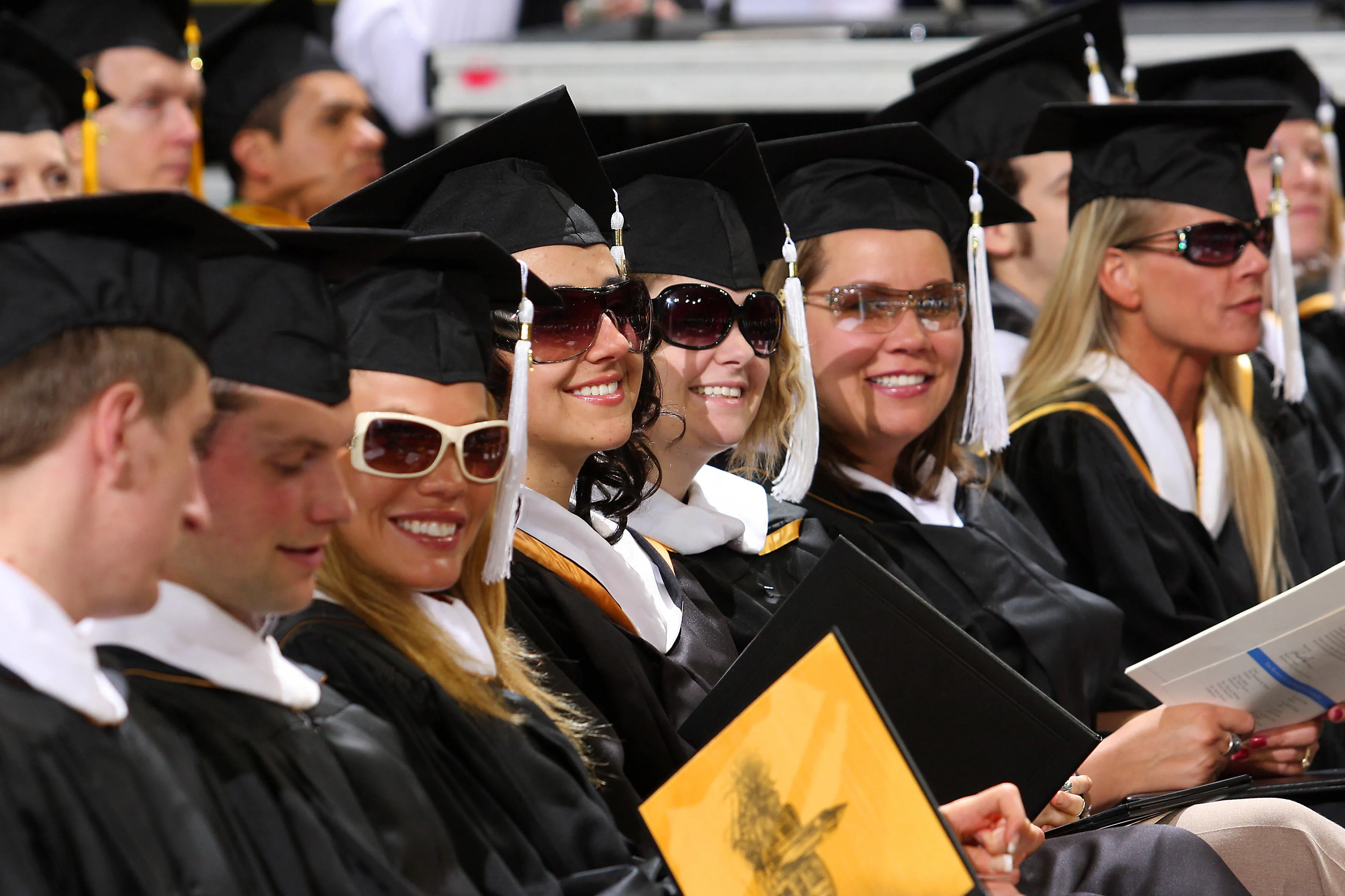 Graduates sitting with caps and sunglasses on.